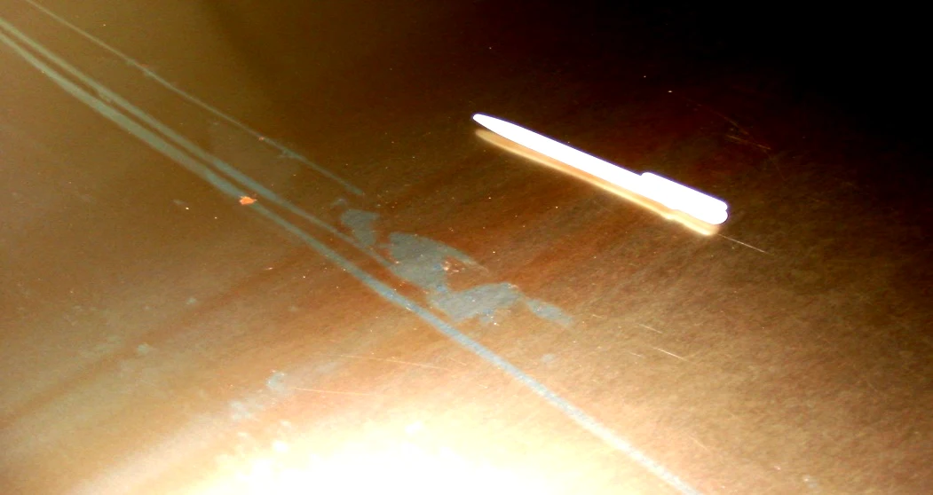 Lackierte Tafel mit unlackierten Schlieren und Stellen, verursacht durch eine verschmutzte Auftragswalze, mit einem Stift als Größenvergleich